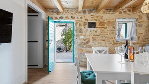 Une cuisine rustique aux murs de pierre, avec des poutres en bois et un coin repas doté de meubles blancs et de verres à vin.