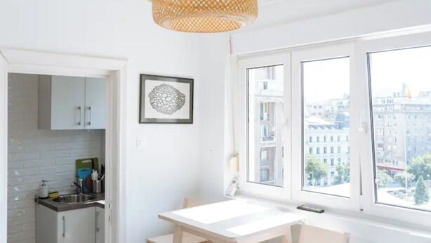 A modern kitchen with white cabinets, a white countertop, and a hanging wicker chandelier.