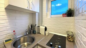 A modern kitchen with white cabinetry, a stainless steel sink, a built-in stovetop, and a window with a view of the sky.