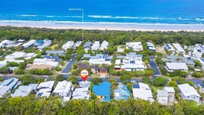 Vista aérea de una zona residencial costera con casas, un acceso a la playa señalizado y un marcador rojo que indica una vivienda específica.