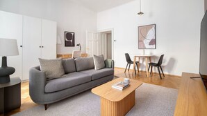 En moderne stue med en grå sofa, et træbord, et spiseområde med et lille bord og stole, samt et hvidt skab.
