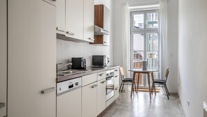 A modern kitchen with white cabinets, a built-in oven, a microwave, and a sink. There is a dining area with a table and chairs, and a window with a view of buildings outside. - Terrific Landstraße 2BR w/ Elevator, nr Tram & Dining, by Blueground (Vienna)