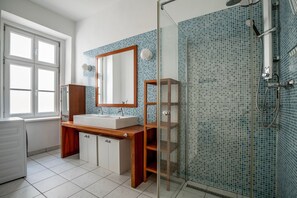 Bathroom features a large window, a wooden vanity with a sink and mirror, and a glass-enclosed shower area.