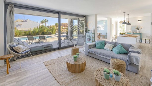 A modern living room with a large sliding glass door leading to a pool area, a grey sofa with green cushions, and a round wooden coffee table. - Casa del Mar · Pool & Sea Views · 10 Guests (Santa Margalida - Can Picafort/Son Serra Marina)