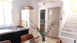 A modern kitchen with a sink, cabinets, and a refrigerator. There is a dining area with a glass table and two chairs. A vase with branches is on the table. - Spectacular duplex with private terrace (Sevilla)