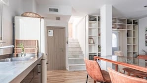 A modern kitchen with a built-in stove, a dining area with a wooden table and two chairs, and a white shelving unit with various items. - Spectacular duplex with private terrace (Sevilla)