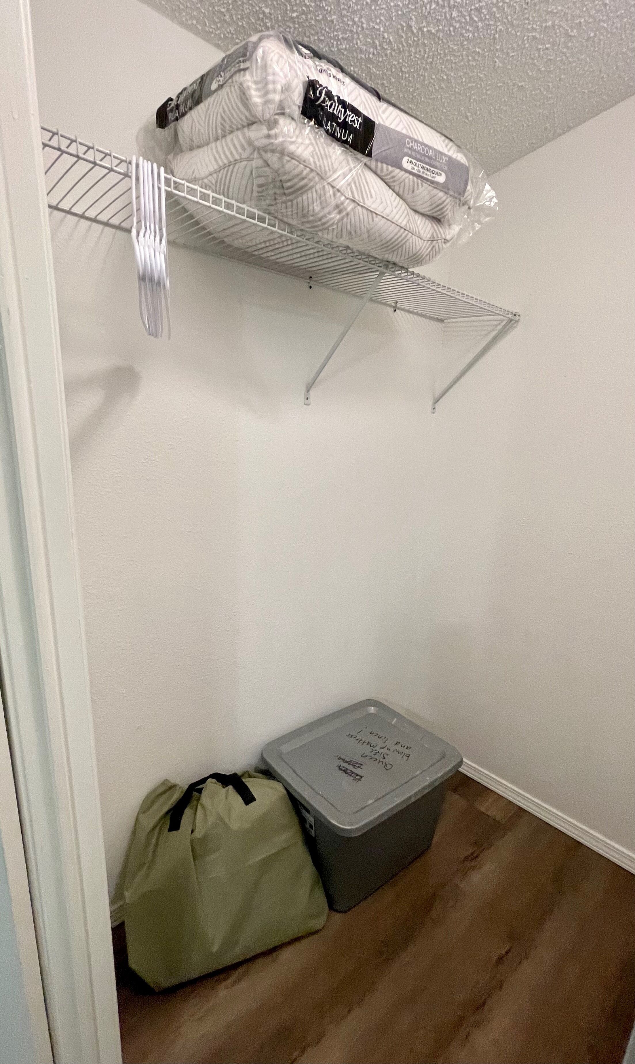 A storage area with a metal shelf holding a mattress and a plastic bin on the floor.
