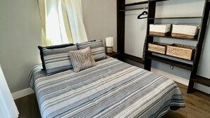 Une chambre à coucher comprenant un lit, un ventilateur de plafond, une fenêtre avec des rideaux et des étagères intégrées avec des paniers.
