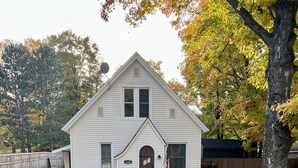 Une maison blanche à deux étages, avec un porche à l’avant, une boîte aux lettres et un drapeau américain.