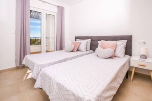 A bedroom with two beds, a nightstand, and a view of the outdoors.