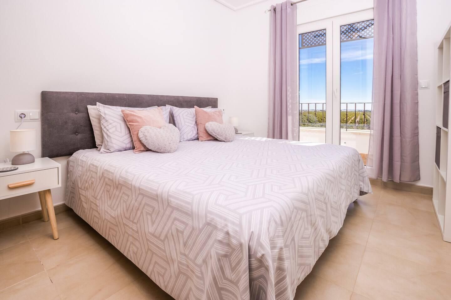 A bedroom with a bed, nightstands, a lamp, and a view of the outdoors through a balcony door.