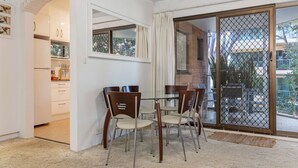 A dining area with a table and chairs, a kitchen in the background, and a sliding glass door leading to an outdoor area. - Oceancrest 11 on Forster main beach. (Forster)