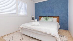 A bedroom with a bed, a nightstand, a lamp, and a window with blinds. - Oceancrest 11 on Forster main beach. (Forster)