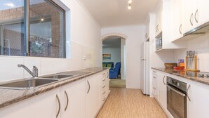 A modern kitchen with white cabinets, a granite countertop, stainless steel appliances, and a window overlooking a brick wall. - Oceancrest 11 on Forster main beach. (Forster)