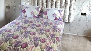 Un dormitorio con colcha y almohada estampadas con motivos florales y una cortina con estampado floral.