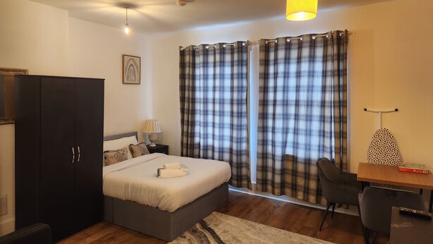 Ein modernes Schlafzimmer mit Bett, Schreibtisch, Stuhl, Kleiderschrank und Vorhängen.