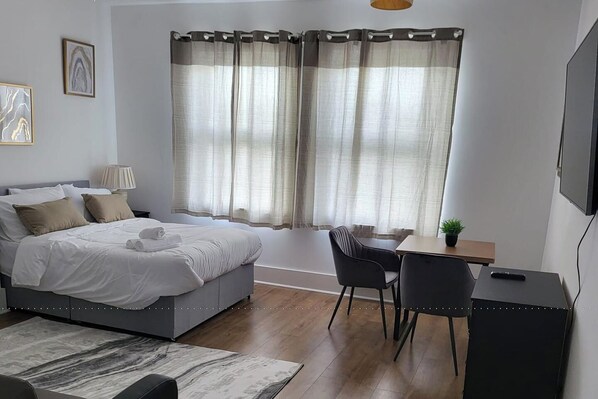 A modern bedroom with a bed, bedside table, lamp, and a desk with chairs. - 1 Bed Flat - Sleeps 3 - Parking - Wifi (Greenhithe)