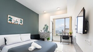Ein modernes Hotelzimmer mit Bett, Schreibtisch, Stuhl und einem großen Fenster mit Blick auf die Stadt.