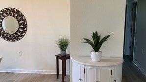 Une pièce avec un meuble blanc, un miroir doté d’un cadre décoratif et deux plantes en pot.