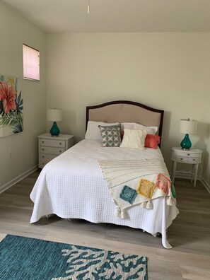 Une chambre à coucher bien aménagée, avec un grand lit, deux tables de chevet avec des lampes, une petite commode et un élément décoratif mural.