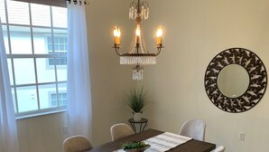 Une salle à manger avec une table en bois, six chaises, un lustre, une plante en pot et un miroir décoratif au mur.