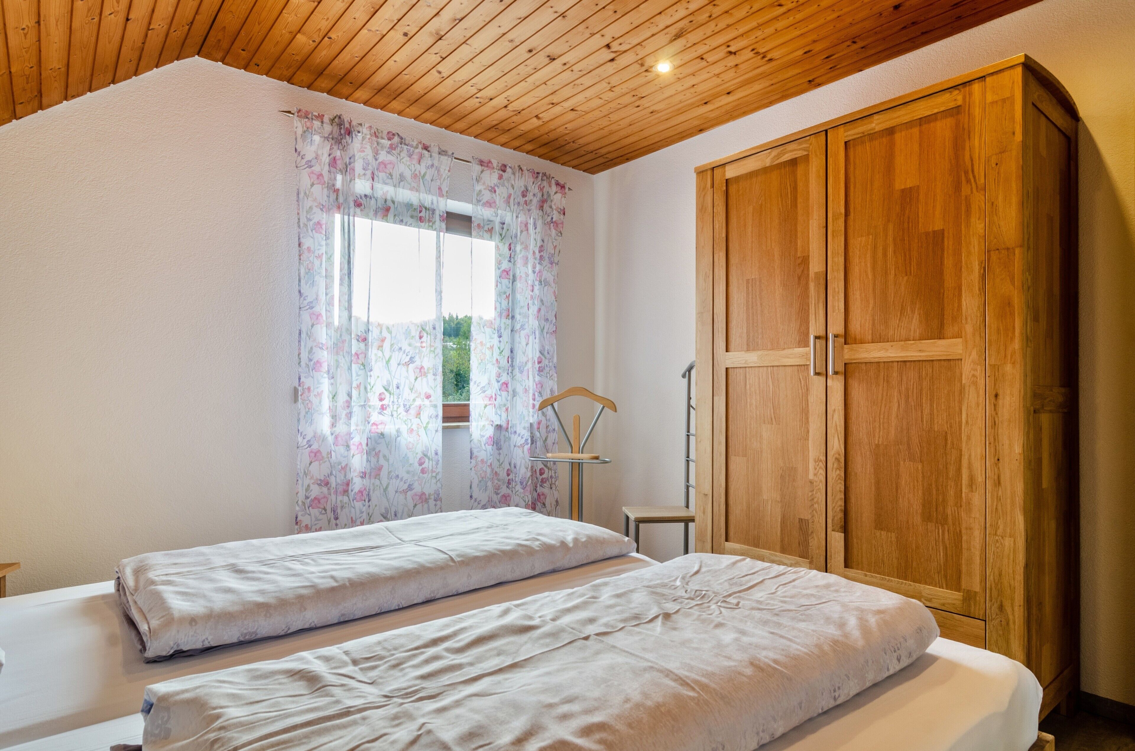 A bedroom with two beds, wooden wardrobe, and a window with floral curtains.