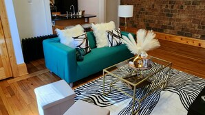 A modern living room with a teal sofa, a zebra-patterned rug, and a glass coffee table. - Chic Coventry — Enjoy 10% off 2+ Nights +Late Check Out  (Cleveland Heights)