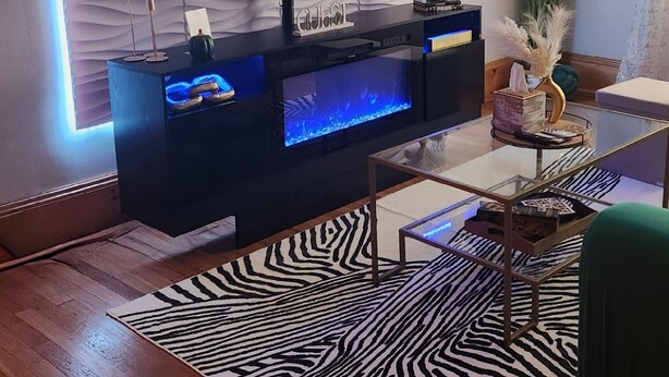 A modern living room with a flat-screen TV mounted on a wall, a wooden entertainment center, and a zebra-patterned rug. - Chic Coventry — Enjoy 10% off 2+ Nights +Late Check Out  (Cleveland Heights)