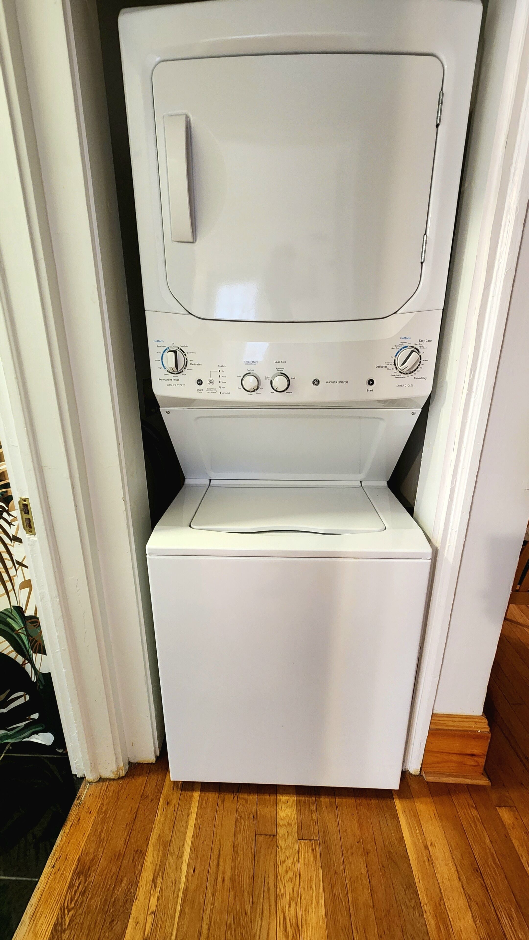 Un appareil compact, blanc, combinant une machine à laver et un sèche-linge à chargement frontal, doté d’un panneau de commande avec de nombreux réglages et boutons.