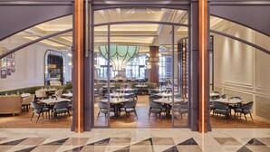 A spacious restaurant with high ceilings, modern chandeliers, and a central decorative column. Tables are arranged in a U-shape, and the floor features a geometric tile pattern. - INSPIRE Entertainment Resort (Incheon)