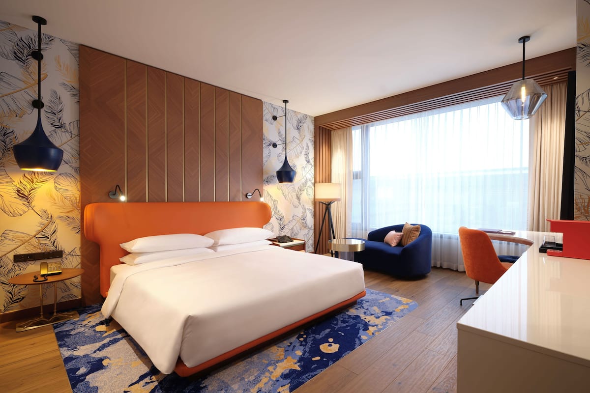 A modern hotel room with a large bed, a desk, a chair, and a sofa.