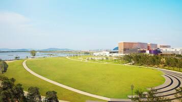 A large, open grassy area with a curved pathway leading to a modern building complex by a body of water.
