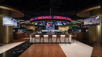 A modern bar area with a large circular screen displaying a basketball game, bar stools, and a counter with a menu.