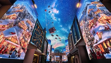 Un centro comercial con grandes pantallas digitales en las paredes que muestran una escena invernal festiva con nieve y adornos navideños.