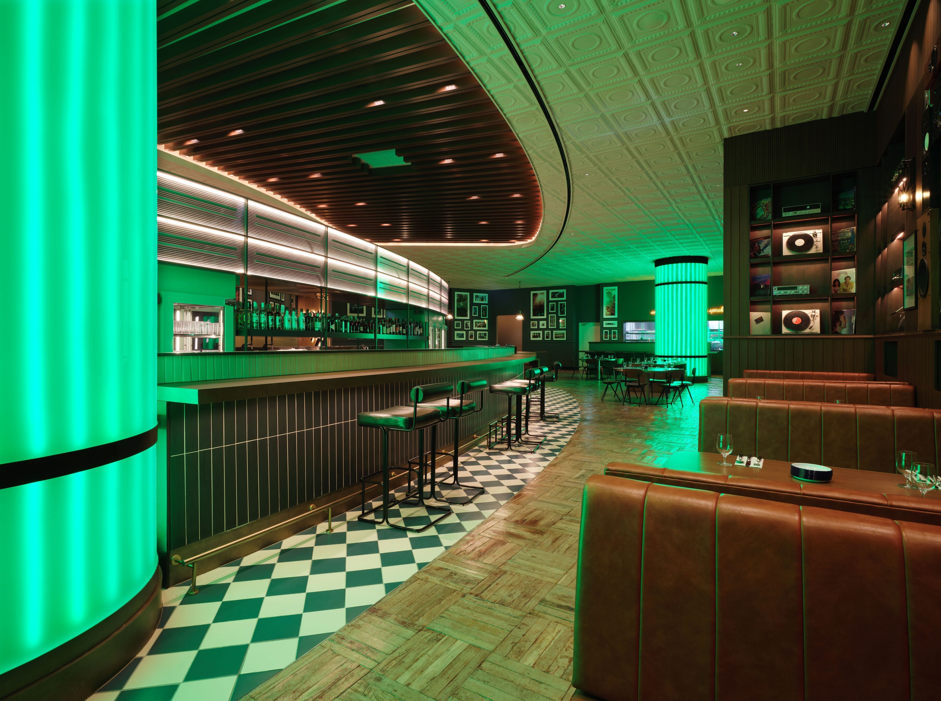 Una zona de bar con suelo a cuadros, iluminación verde y asientos de cuero.