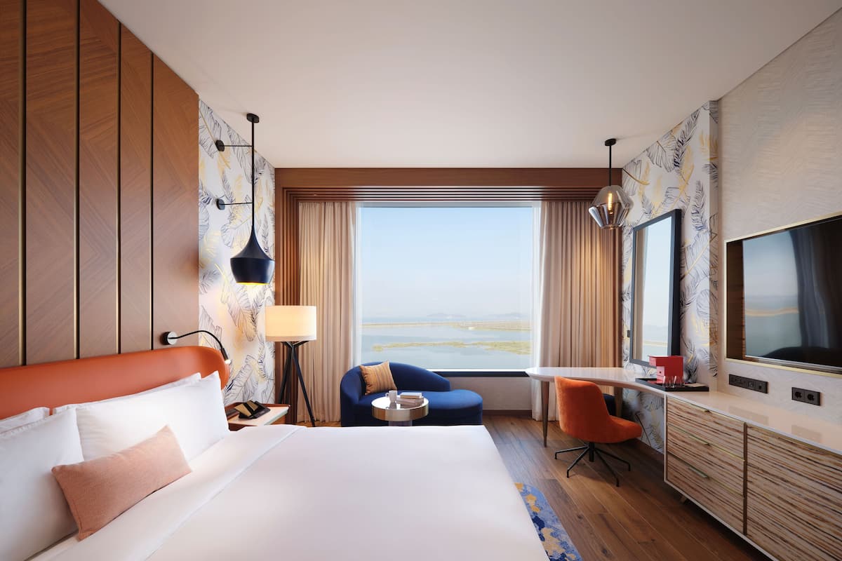 A hotel room with a large bed, a desk, a chair, and a TV.