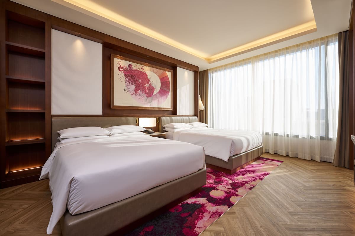 A hotel room with two beds, a large abstract painting, a wooden floor, and a large window with curtains.