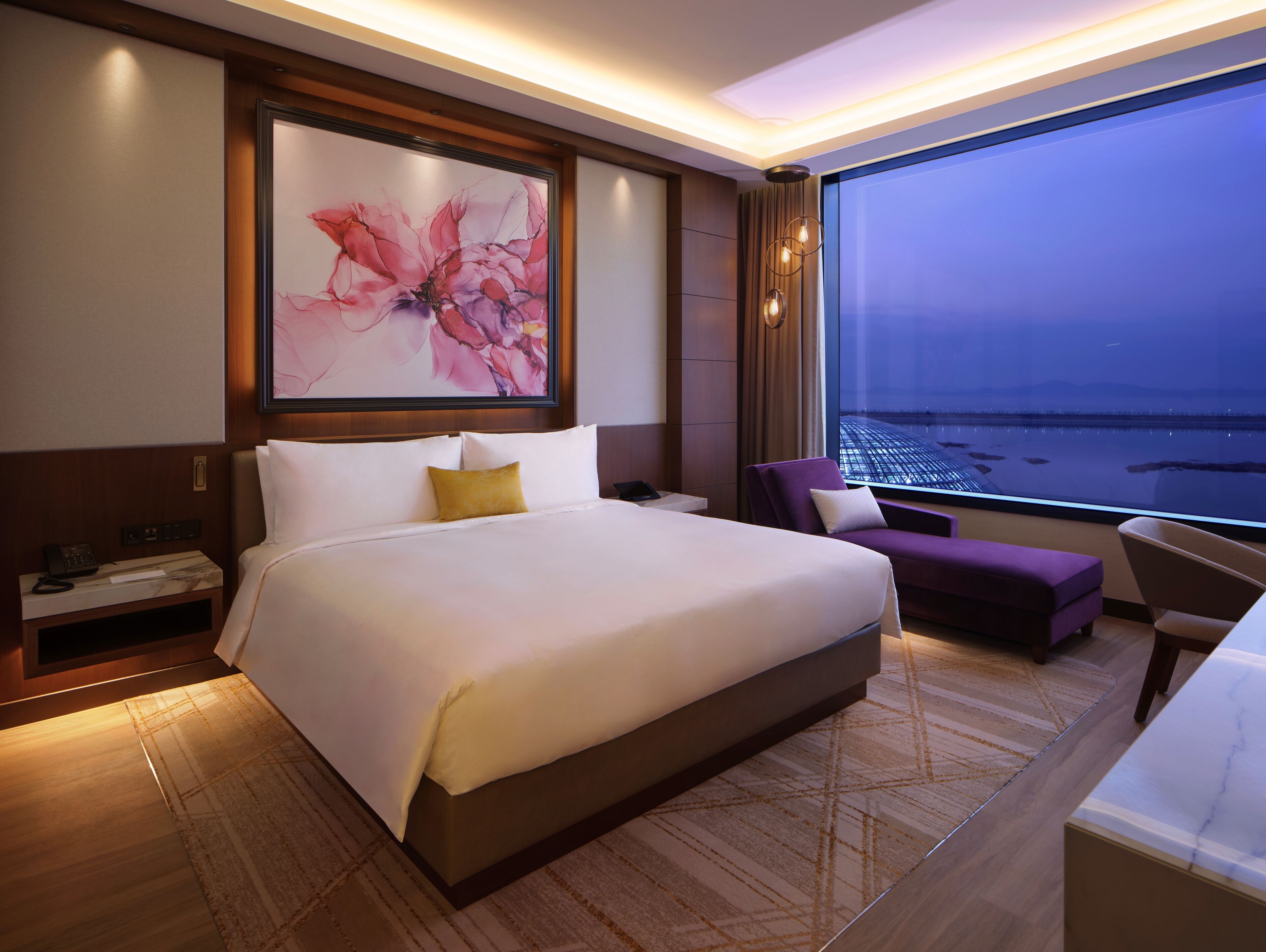 Une chambre d’hôtel avec un grand lit, un bureau, une chaise, une table de chevet et une grande fenêtre donnant sur l’eau.