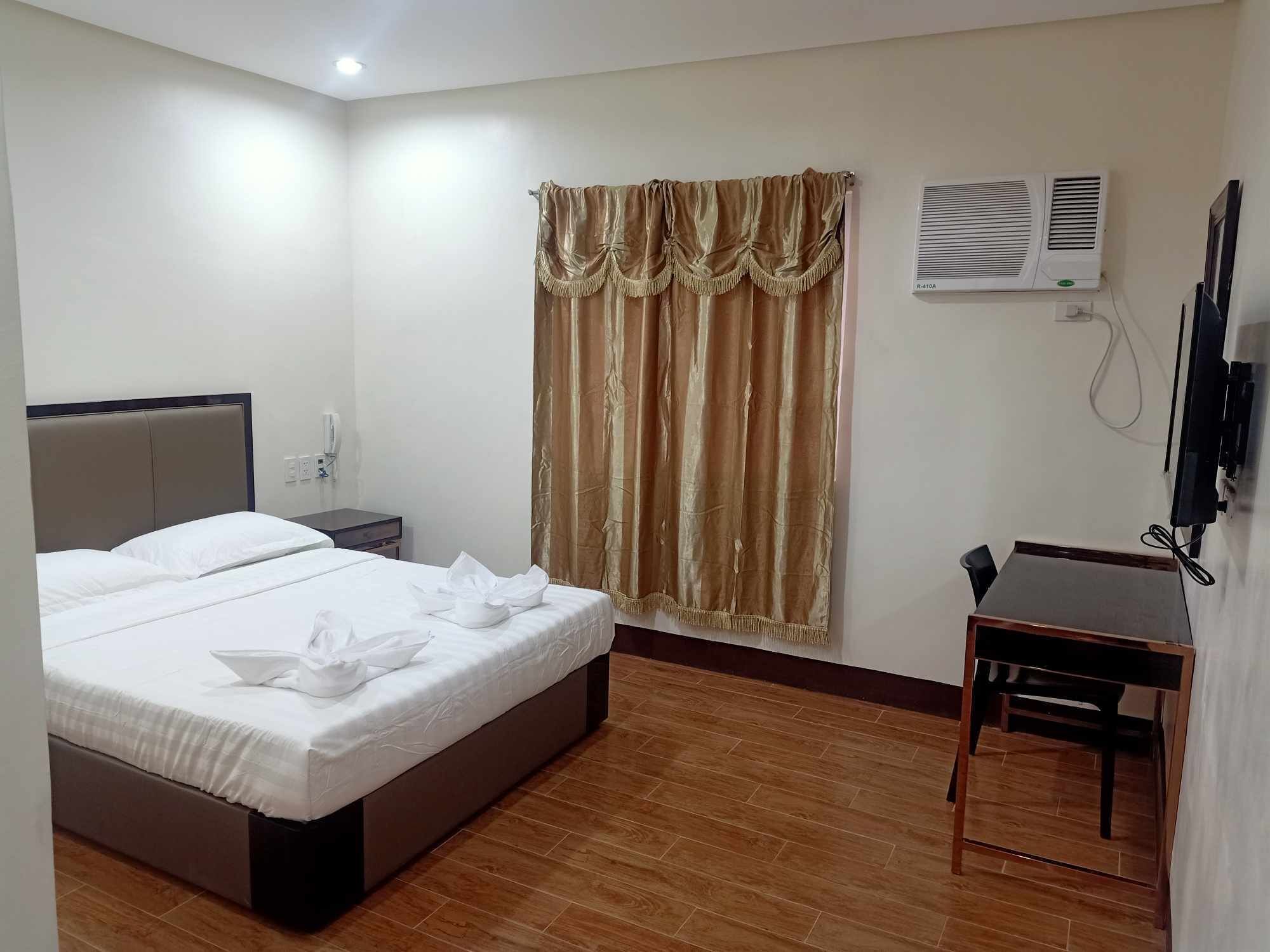A hotel room with a bed, bedside table, and a desk with a chair.
