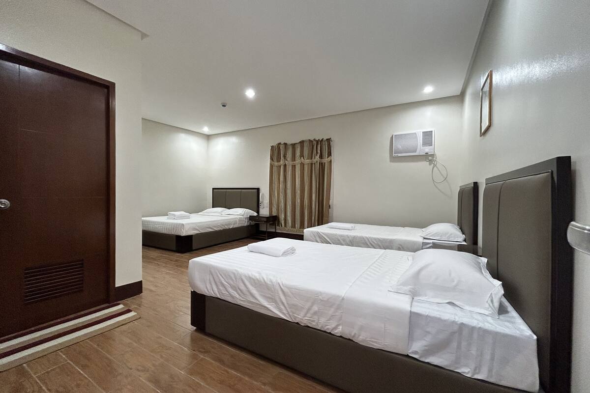 A hotel room with two beds, a wardrobe, a bedside table, a wall-mounted air conditioner, and a curtain.