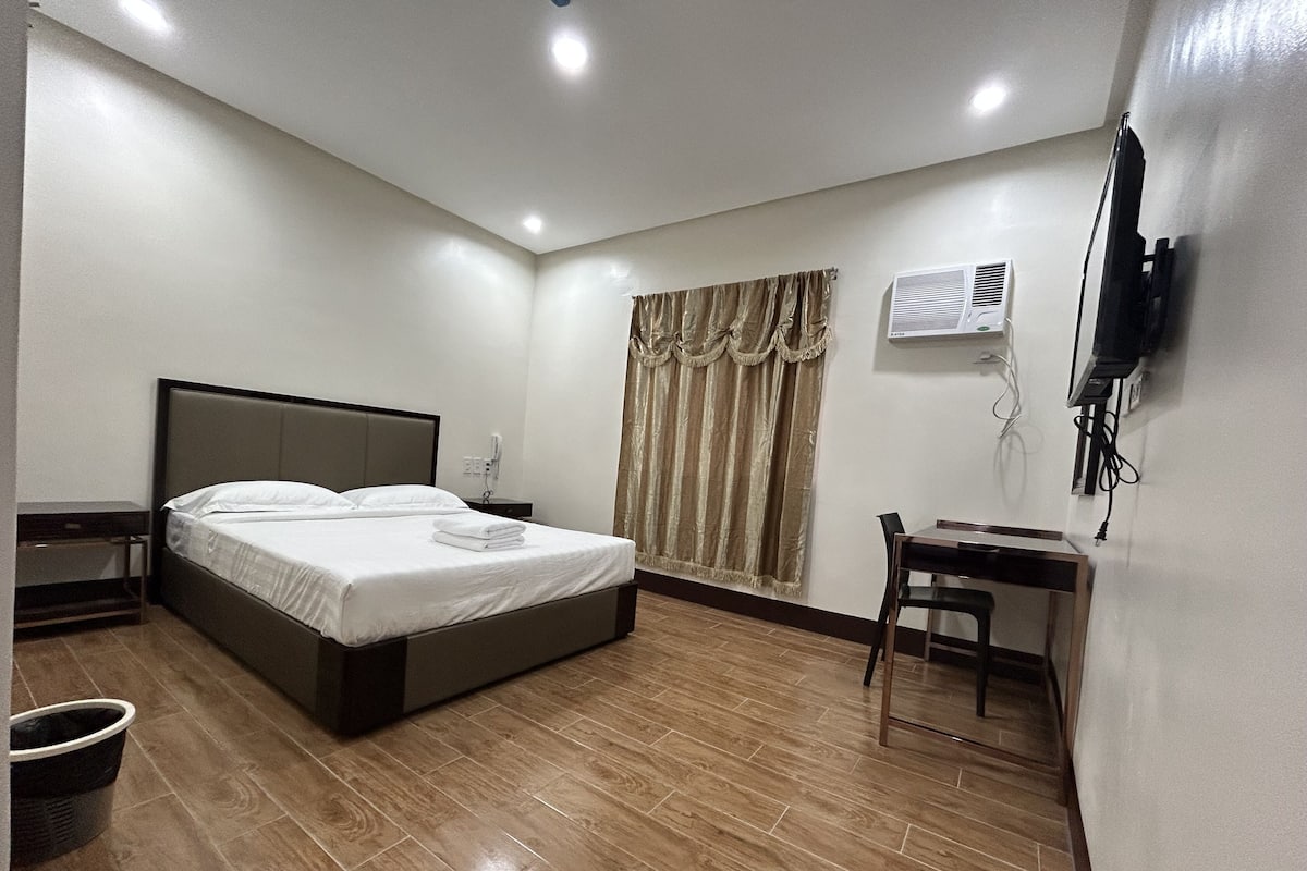 A hotel room with a bed, a desk, a chair, a television, and a window with curtains.
