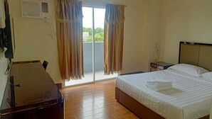 A hotel room with a bed, a desk, a chair, a TV, and a sliding glass door to the outside. - Asia Jem Hotel-Gapan City (Gapan City)