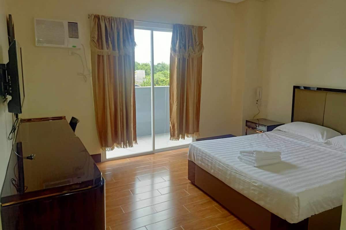 A hotel room with a bed, a desk, a chair, a TV, and a sliding glass door to the outside.