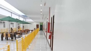A long, narrow hallway with a yellow railing on one side, a white marble floor, and a green umbrella-covered seating area on the other. - Asia Jem Hotel-Gapan City (Gapan City)
