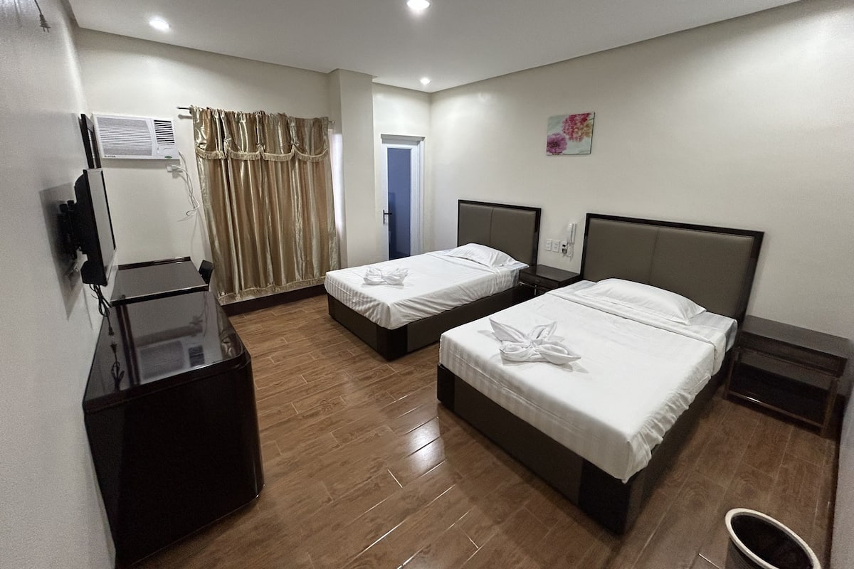 A hotel room with two single beds, a desk, a TV, and a bathroom.
