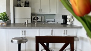 A modern kitchen with white cabinets, a central island with stools, and a dining table set for two.