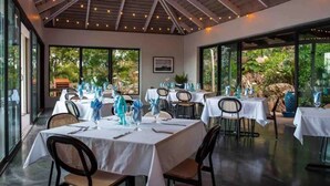 A restaurant with tables set for dining, large windows, and a ceiling with exposed beams and string lights.