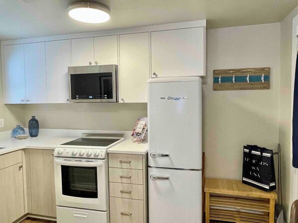 A compact kitchen with white cabinets, a microwave, a stove, and a refrigerator. - Edmonds Getaway Cottage | Walk to Train & Stadium (Edmonds)