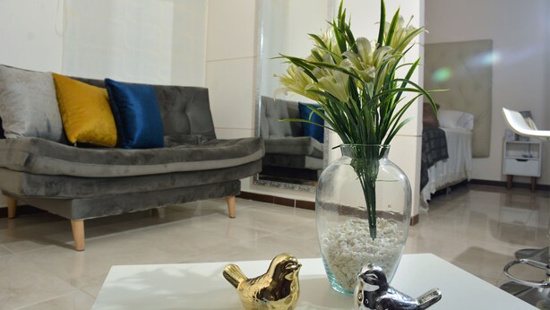 Ein modernes Wohnzimmer mit einem grauen Sofa, einer Blumenvase und einer goldenen Vogelstatue auf einem weißen Tisch.