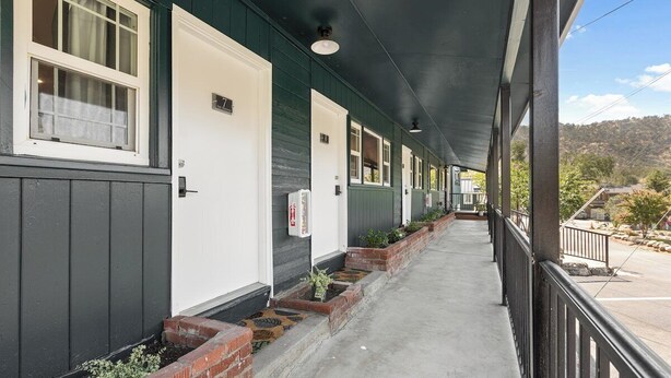 A covered corridor with doors numbered 7 to 10, a fire extinguisher, and a view of the surrounding landscape. - The Belle Sequoia Motel RM9 (Three Rivers)